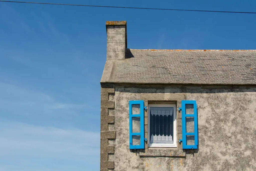 Maison en pierre aux volets bleus sous un ciel dégagé, en Bretagne